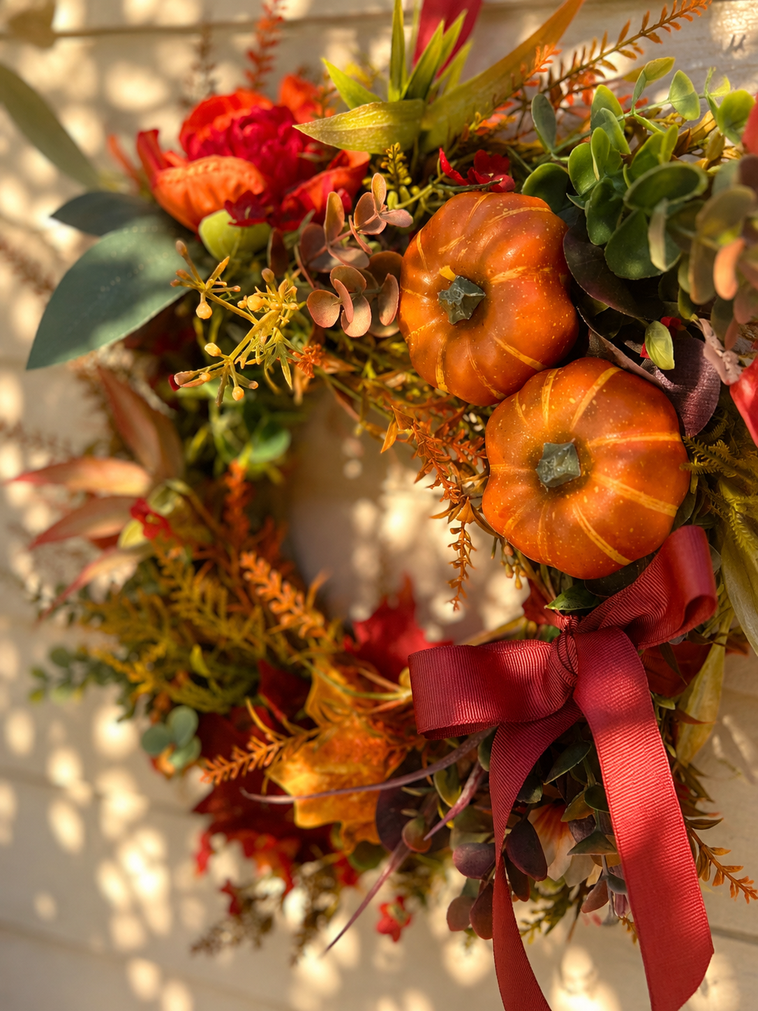 Close up of The Harvest wreath showing mini pumpkins, berries and burgundy ribbon bow detail